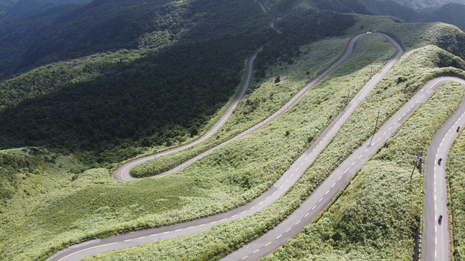 Aerial view of a winding switchback mountain road curving through green hills