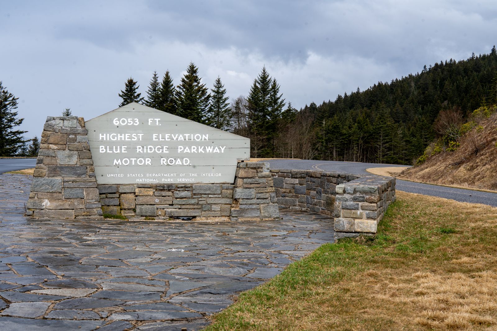 Stone elevation marker for the Blue Ridge Parkway at 6,053 feet, beside a winding mountain road through forest