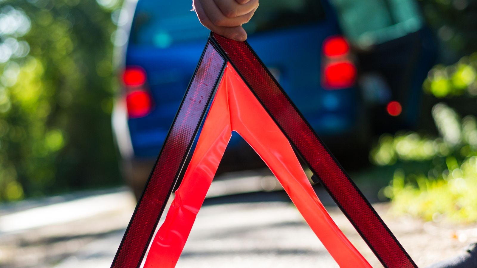 A hand placing a reflective warning triangle behind a stopped van