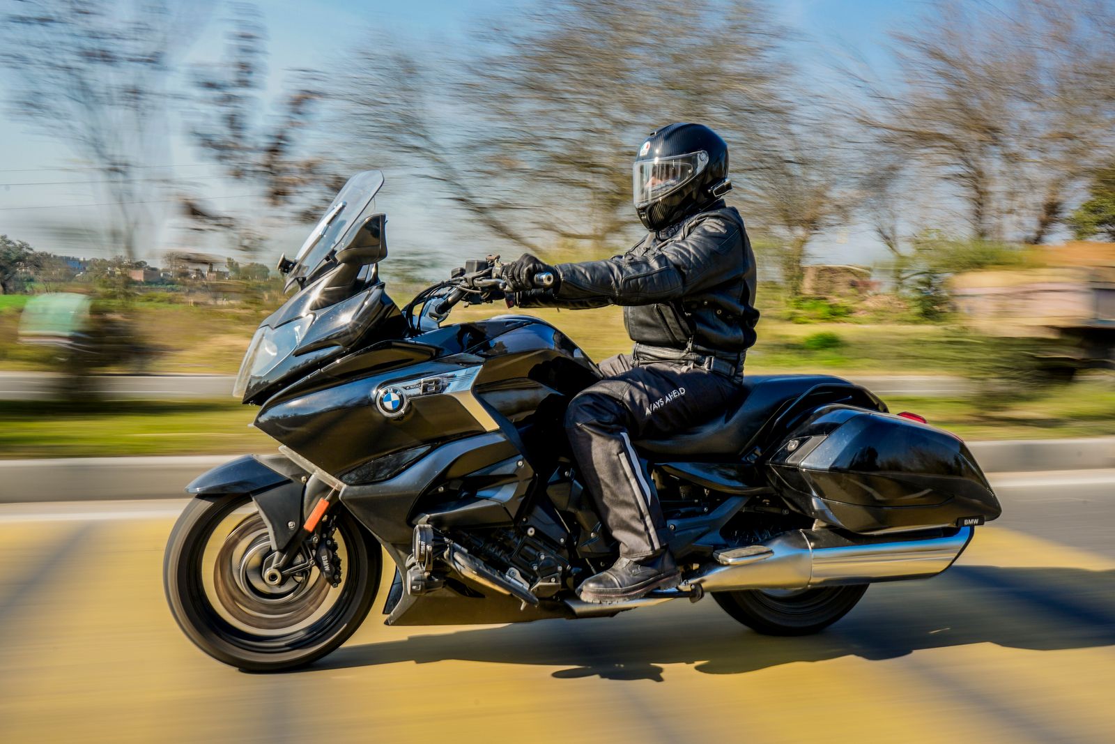 A motorcyclist in full riding gear on a black touring motorcycle, riding down a road with motion blur in the background