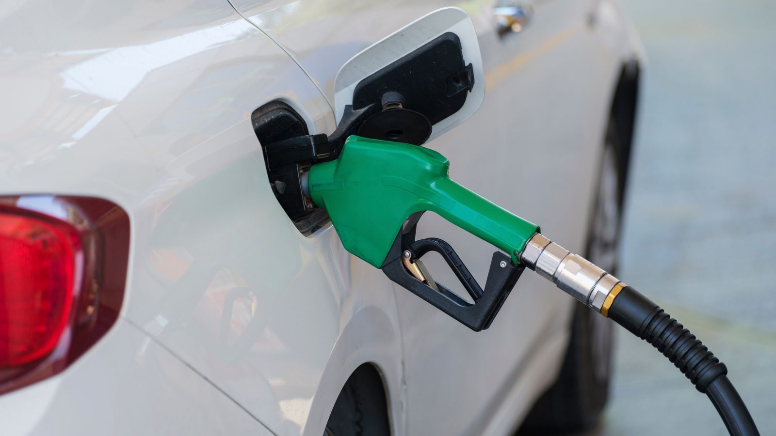 A green fuel nozzle refueling a white car at a gas station