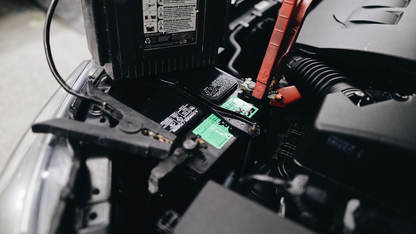 Jumper cables clamped to a car battery under the hood